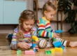 Niños pequeños jugando en el suelo con bloques de construcción de colores de tamaño grande para fomentar la creatividad.