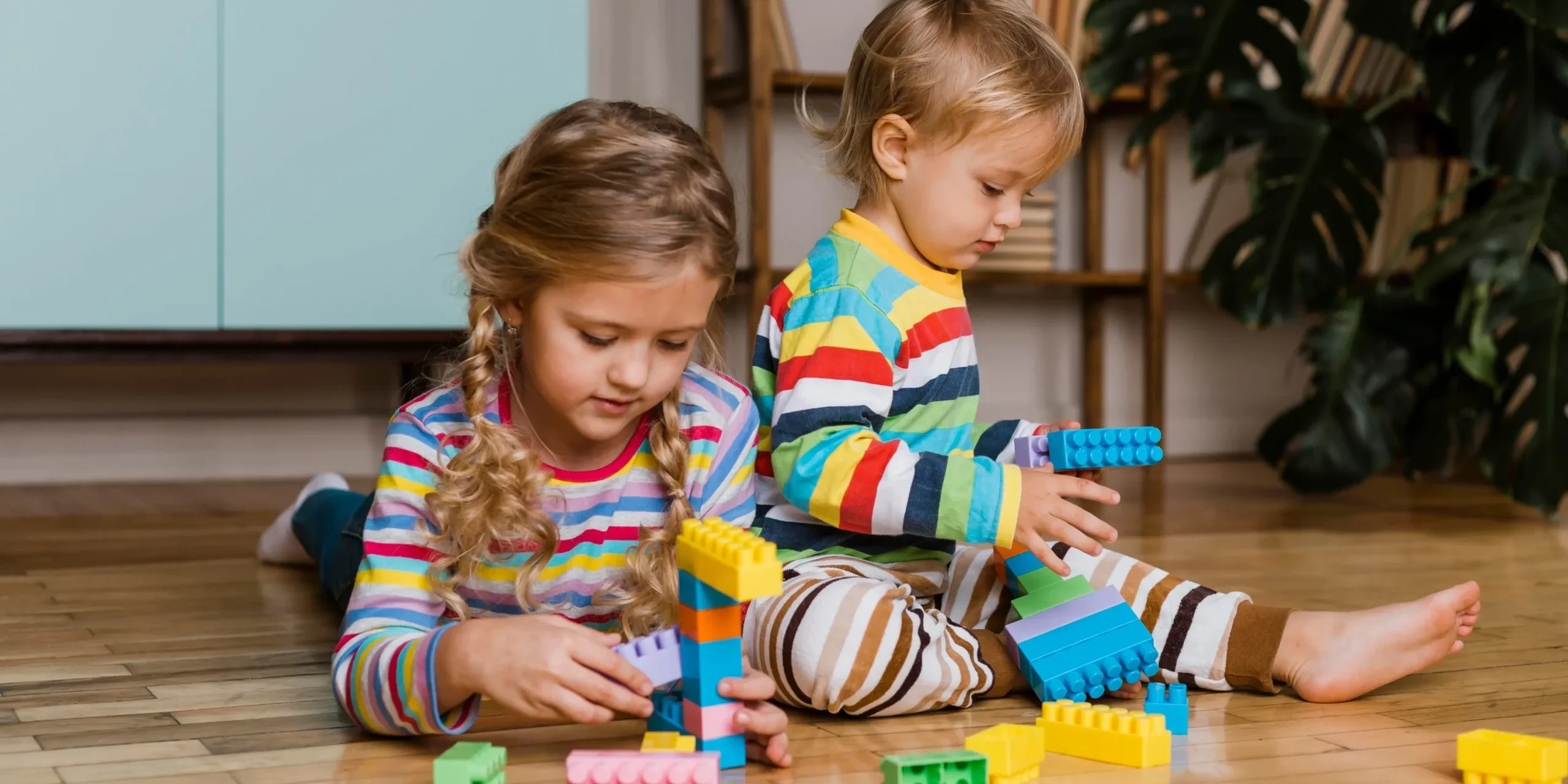 bloques-construccion-grandes-ninos-preescolar Niños pequeños jugando en el suelo con bloques de construcción de colores de tamaño grande para fomentar la creatividad.